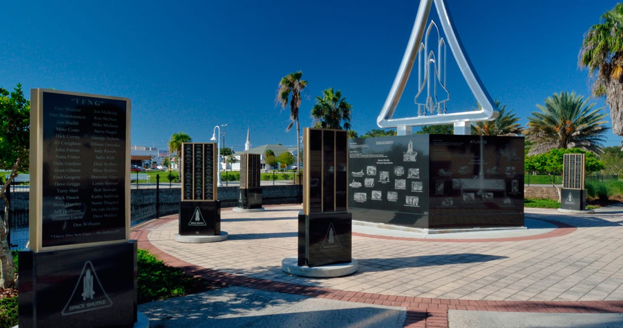 Space Shuttle Monument plaza beneath a blue sky and palm trees.